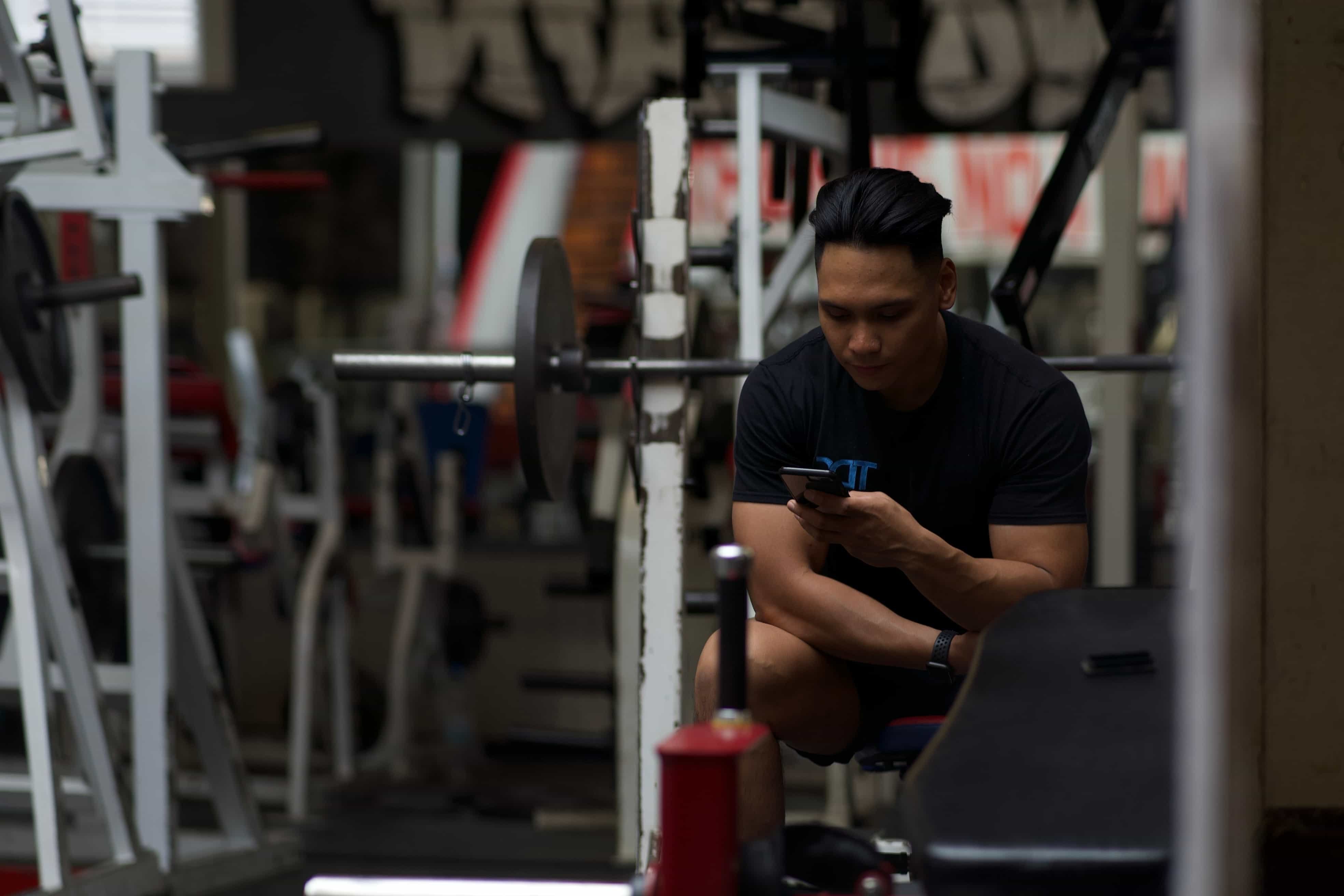 An image of Thom looking at his phone while sitting on a bench machine